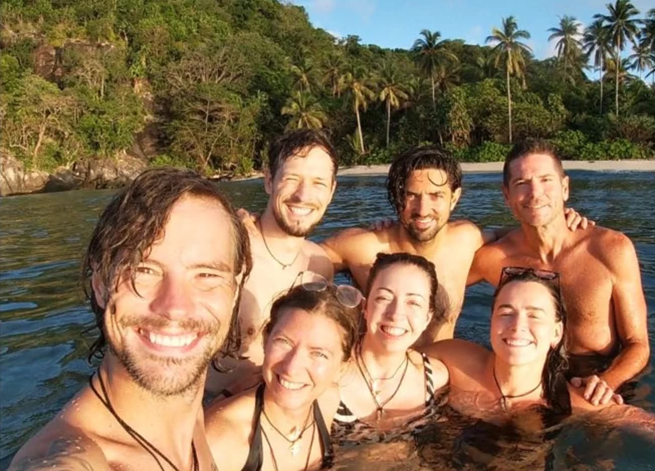 Tommy in the foreground and Steve in the back row, with friends in the sea beside a palm-covered island in Indonesia.