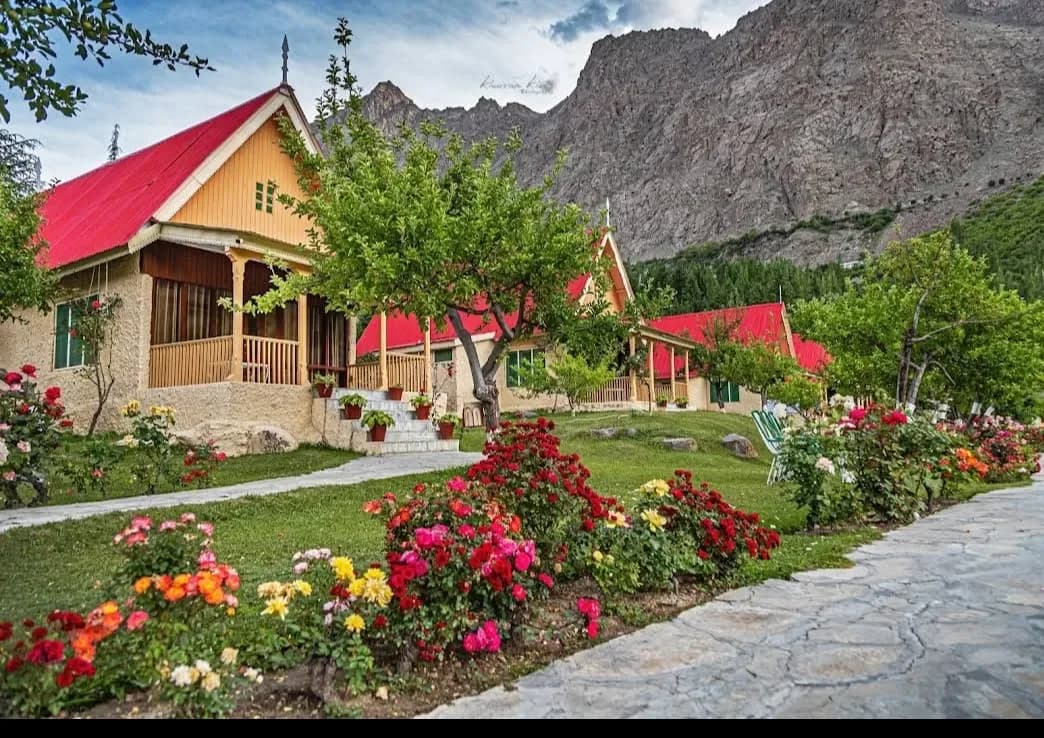 Red-roofed cabins and flower gardens beside a stone path, with rocky slopes behind.