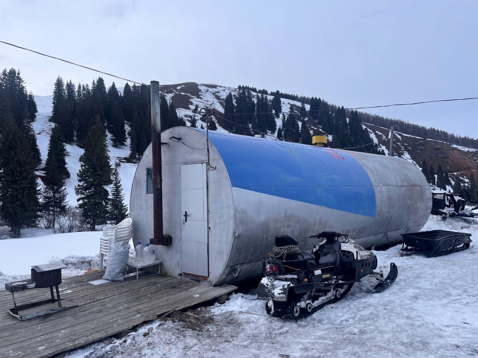A bar built into an abandoned fuel tank on a snowy hillside, a snowmobile parked outside.