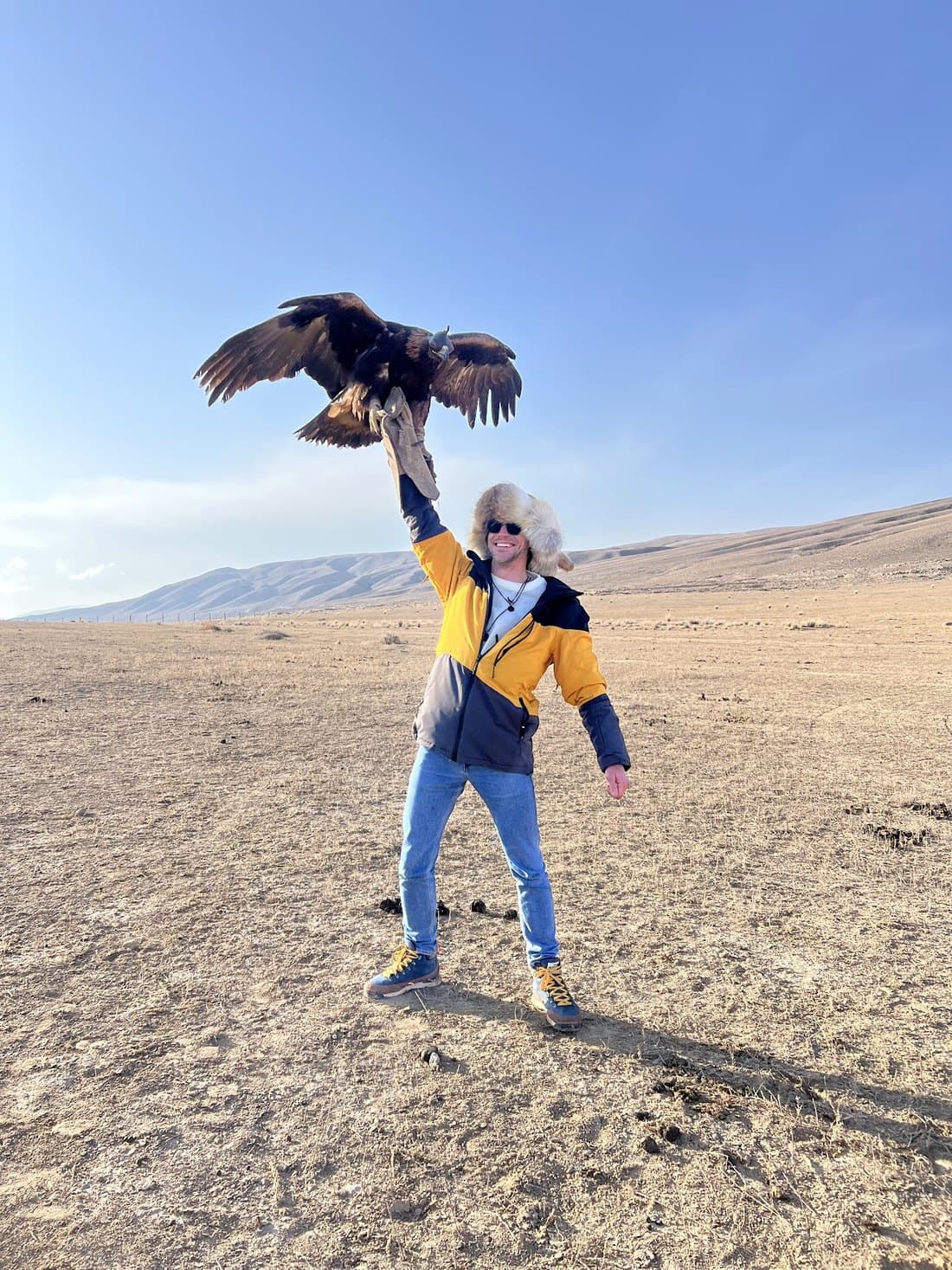 A traveller on the steppe holding a golden eagle on a gloved fist, its wings fully spread.